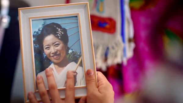 Screen capture from The Bureau of Magical Things, a hand holding a framed photo of a smiling Japanese woman